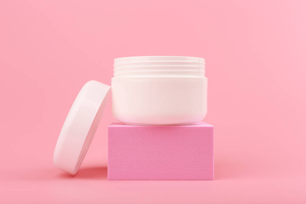 Close up of face cream. mask or balm in white jar with opened cap on pink podium against pink background - Foto, immagini