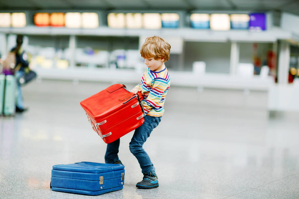 Glücklicher kleiner Junge mit großem Koffer am Terminal des internationalen Flughafens. Aufgeregtes Kind im Vorschulalter wartet auf Flug und Urlaub. Lebensstil der Familie. - Foto, Bild