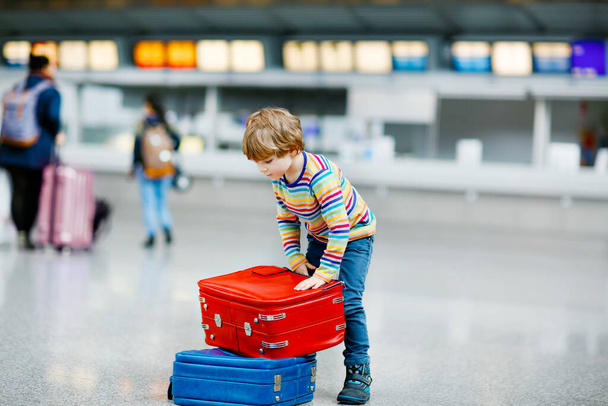 Happy little kid boy with big suitcase luggage at terminal on international airport. Preschool excited child wait for flight and going on vacations. Travel family lifestyle. - 写真・画像