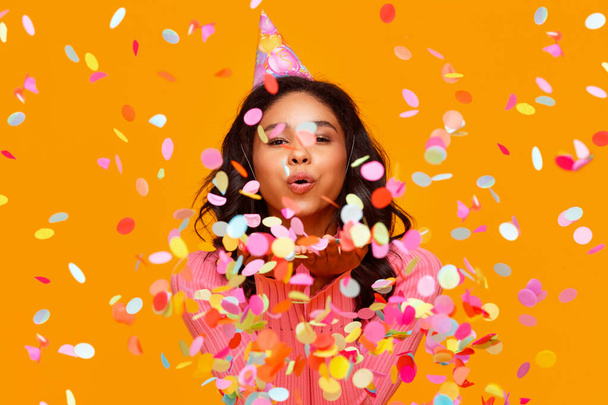 happy birthday! cheerful funny young ethnic woman with festive confetti on yellow background - Фото, зображення