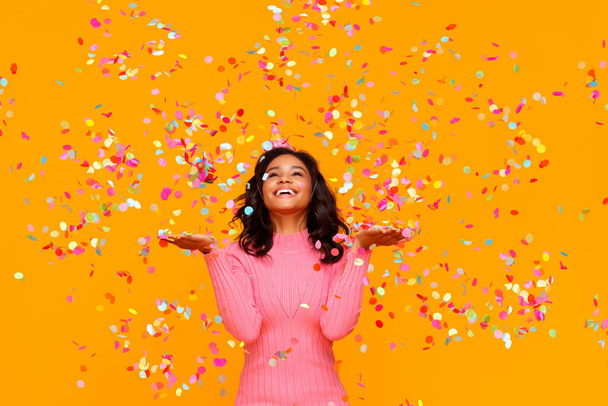 happy birthday! cheerful funny young ethnic woman with festive confetti on yellow background - Photo, Image