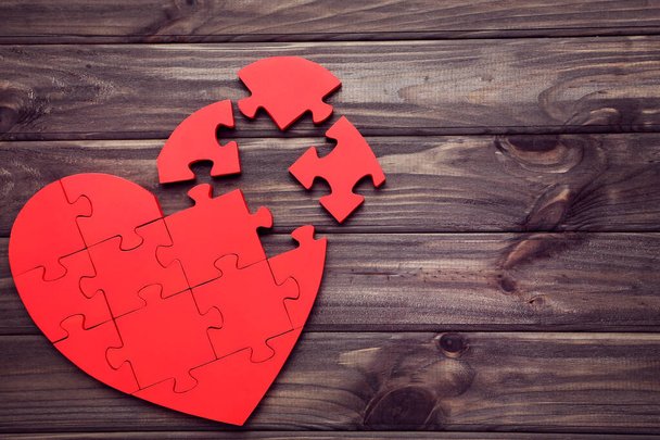 Broken puzzle heart on brown wooden table - Фото, изображение
