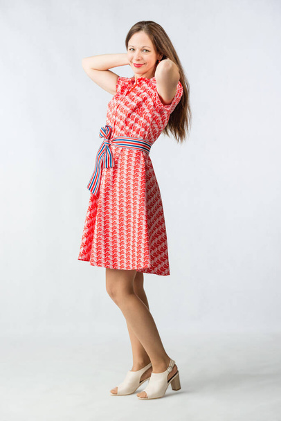 Νεαρή χαρούμενη γυναίκα με κόκκινο φόρεμα ποζάρει στο στούντιο σε λευκό φόντο - Φωτογραφία, εικόνα