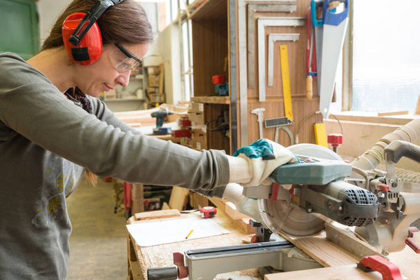 Young woman cutting a wooden plank with a circular saw in a workshop - Photo, Image