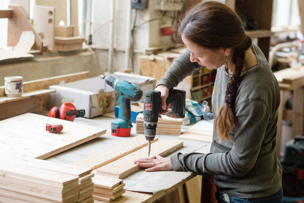 Junge Frau mit Elektroschrauber auf Holzstück in Werkstatt - Foto, Bild