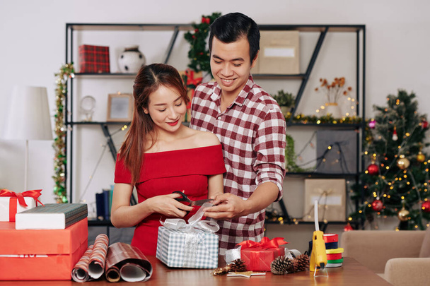 Young Asian couple in love wrapping and decorating Christmas presents for holiday season together - Фото, зображення