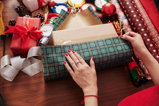 Process of wrapping Christmas present in green plaid wrapping paper - 写真・画像