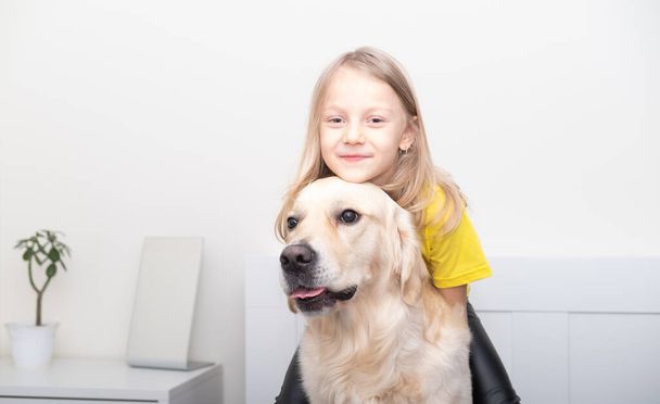 Uma menina de t-shirt amarela abraça um cão na cama. Golden Retriever está brincando com uma criança. Tendência de cores de 2021 cinza e amarelo. - Foto, Imagem