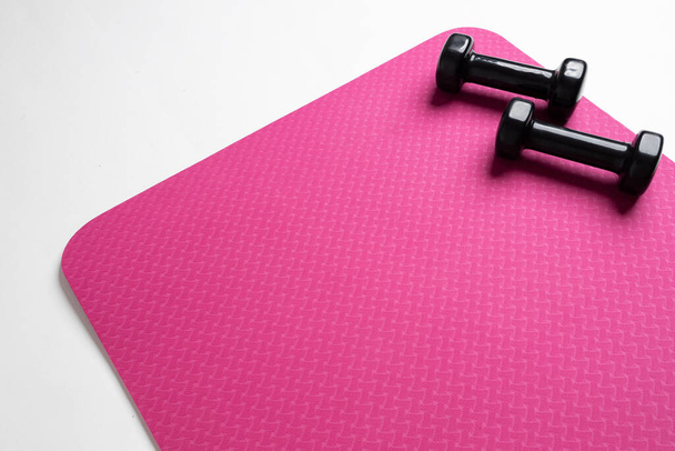 A top view of a pink fitness mat and two black dumbbells isolated on a white background - Foto, imagen