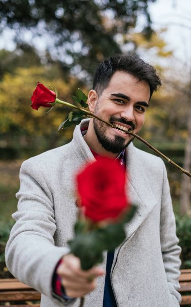 A vertical closeup of a male holding and biting the stem of red roses-concept Valentine's day - Photo, Image