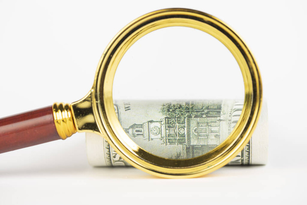 A closeup shot of a magnifying glass viewing a bundle of 100 dollar bills on white background - Fotó, kép