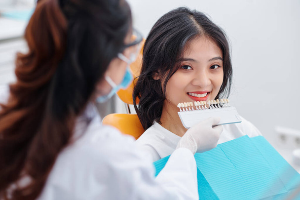 Стоматолог выбирает цвет зубов пациента с палитрой в клинике - Фото, изображение