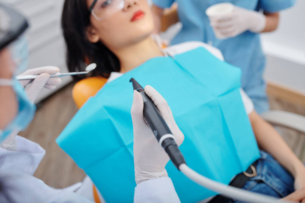Zahnarzt in Einmalhandschuhen mit kleinem Spiegel und Bohrer bei der Behandlung von Hohlräumen bei jungen Patientinnen - Foto, Bild
