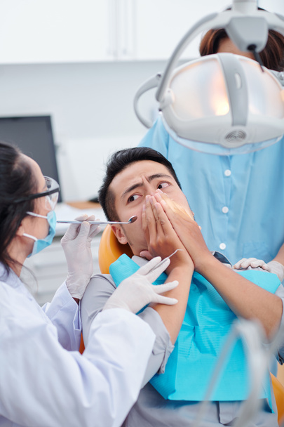 Dentista pidiendo paciente asustado para calmarse y dejar de cubrir su boca para que ella pudiera comprobar sus dientes - Foto, imagen