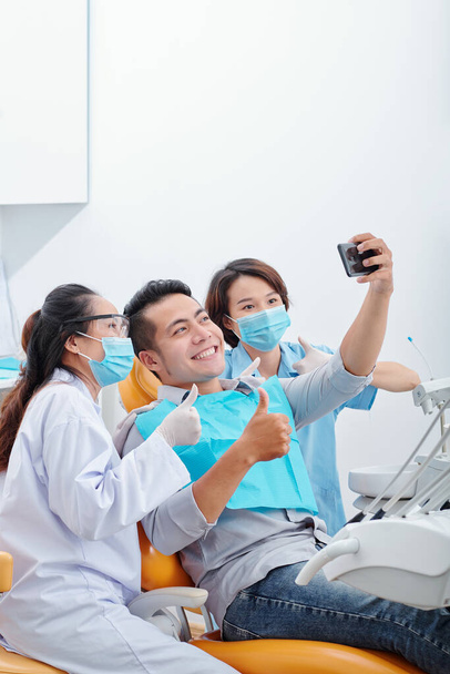 Glücklich aufgeregten asiatischen Mann lächelnd und Selfie mit Zahnarzt und Assistentin - Foto, Bild