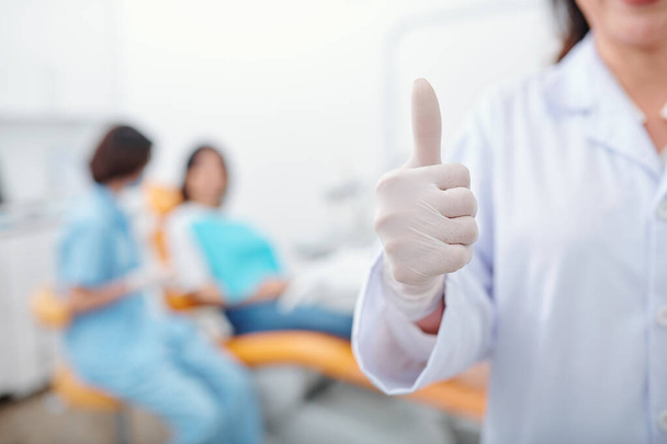 Imagem cortada de dentista em luva de látex mostrando polegares para cima após o tratamento da cavidade de acabamento - Foto, Imagem