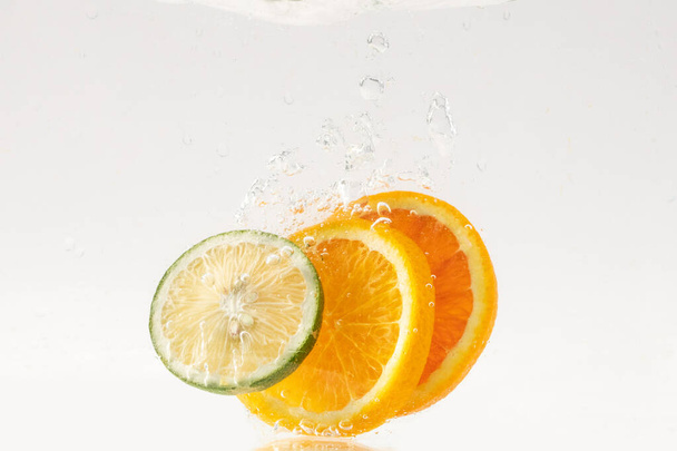 Citrus slices floating in bubbling water on white surface - Fotografie, Obrázek