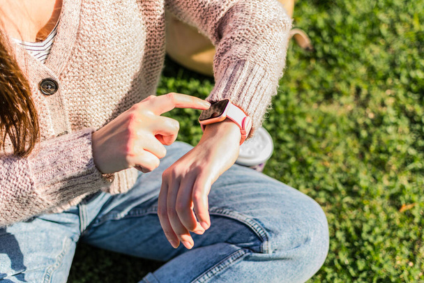A close-up of a woman's hands checking the time on a smart watch sitting in a park - Foto, Imagen