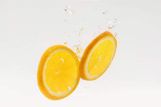 Lemon slices bubbling in water on white background - Valokuva, kuva