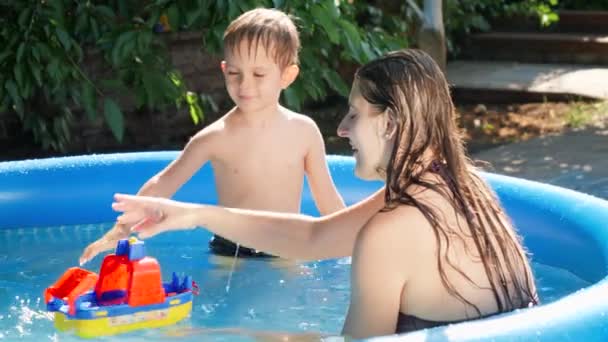 Küçük tatlı bir çocuk ve genç bir anne oyuncak gemi ya da tekneyle havuzda oynuyorlar. Mutlu ve neşeli aile kavramı yaz tatili ve tatil - Video, Çekim