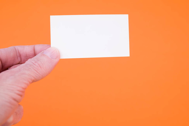A closeup shot of a person holding a blank paper on an orange background - Φωτογραφία, εικόνα