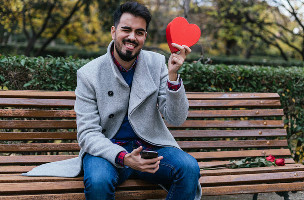 A vertical closeup of a male holding a red heart on a bench outdoors-concept Valentine's day - Fotografie, Obrázek