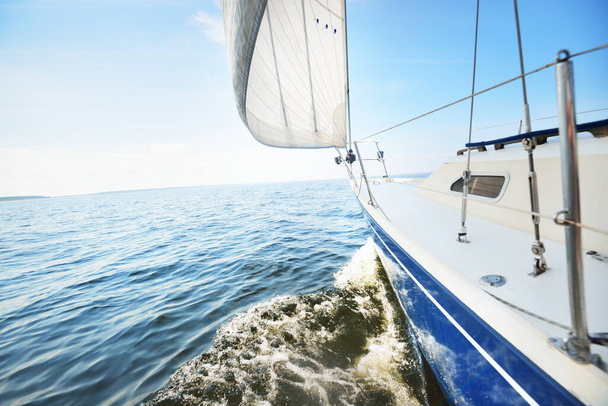 Bílá jachta pluje za slunečného letního dne. Pohled shora dolů z paluby na příď a plachty. Vlny a šplouchání vody. Jasné modré nebe. Baltské moře, Švédsko - Fotografie, Obrázek