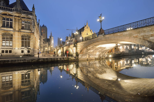 Illuminated promenade near St Michael bridge and St Bavo's Cathedral in a historical center of Ghent city. Night cityscape. Symmetry reflections on the water. Travel guide, sightseeing theme. Belgium - Photo, Image