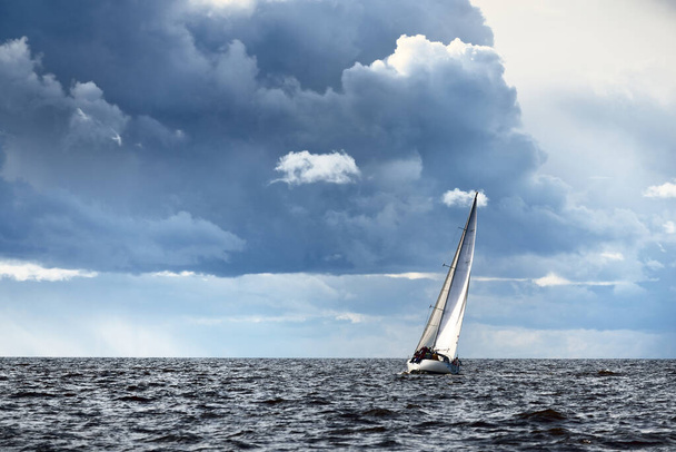 Vitorlás jacht regatta. Modern vitorlás száguld át a hullámokon. Drámai égbolt a vihar előtt. Óriási felhő. Észak-Németország, Kiel - Fotó, kép