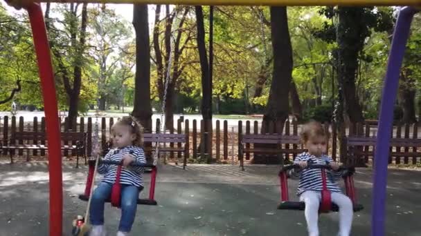 Dos niñas pequeñas, jugando en el patio. Hermanas gemelas fraternales, balanceándose en un columpio - Metraje, vídeo