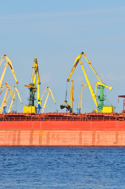 Riga Limanı, Letonya 'da büyük kırmızı bir yük gemisi yükleniyor. Yattan bir manzara. Küresel iletişim, lojistik, endüstri, nakliye - Fotoğraf, Görsel