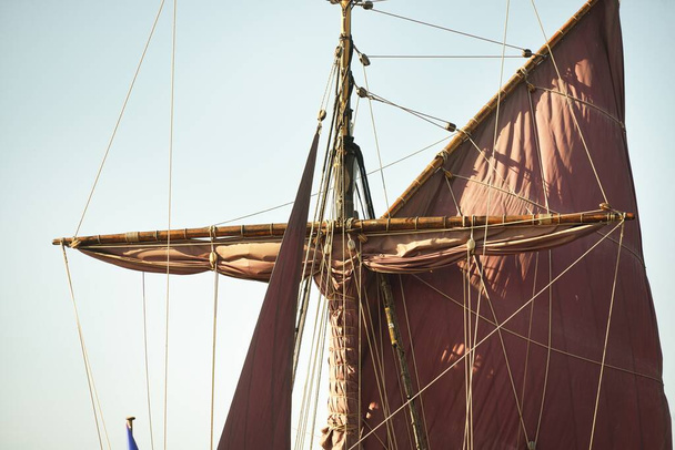 Mast, rode zeilen en tuigage van een oud klassiek zeilschip uit de 18e eeuw, close-up. Heldere blauwe lucht - Foto, afbeelding