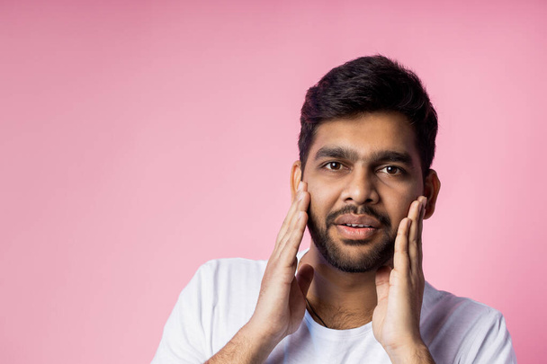 Stunned handsome unshaven indian male, being shocked by low prices on sale, keeping hands on cheeks, opening mouth in surprise, isolated over pink background. Emotions, reactions concept. Copy space. - Fotografie, Obrázek