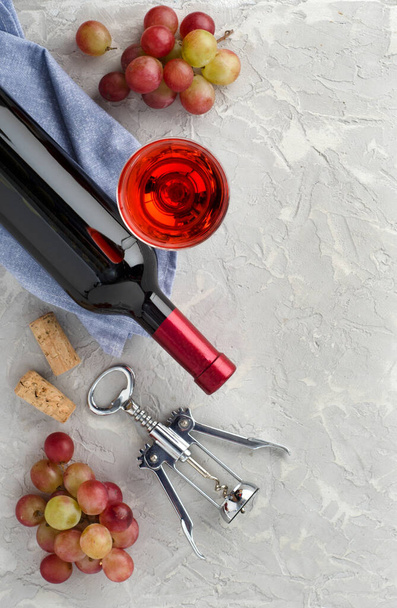 ワインボトル、ワイングラス、ピンクのブドウの束とあなたのテキストのためのコピースペースとグレーのテクスチャの背景に金属製のコルクねじ。平置きだ。トップ表示. - 写真・画像