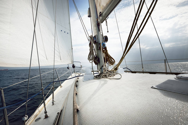 Weiße Jacht segelt an einem sonnigen Sommertag. Nahsicht vom Deck auf Bug, Mast und Segel. Wellen und Wasser plätschern. Strahlend blauer Himmel. Finnischer Golf - Foto, Bild