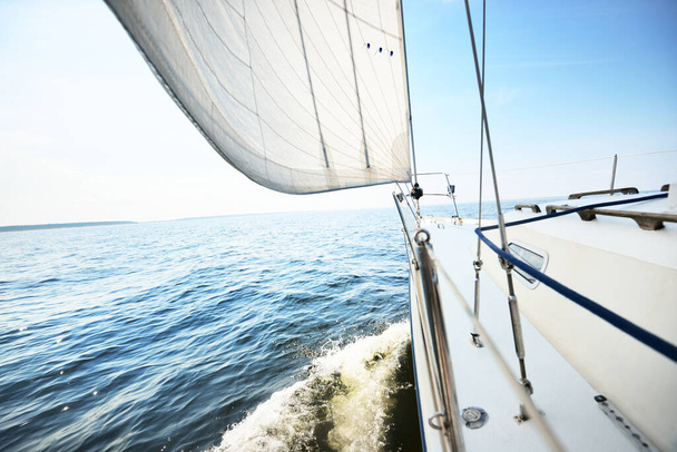Белая яхта плавает в солнечный летний день. Вид крупным планом с палубы на лук и паруса. Волны и брызги воды. Ясное голубое небо. Балтийское море, Швеция - Фото, изображение