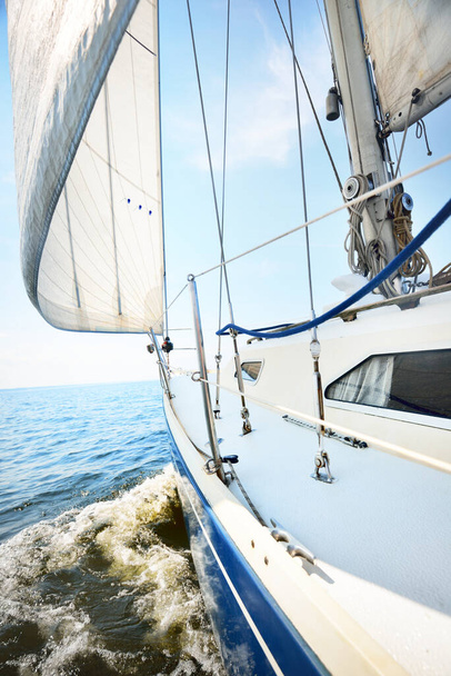 Fehér jacht vitorlázás egy napos nyári napon. Közelkép a fedélzetről az orrra és a vitorlákra. Hullámok és vízcsobbanások. Tiszta kék ég. Balti-tenger, Svédország - Fotó, kép
