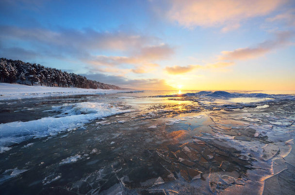 Panorámás kilátás a fagyott Balti-tenger partján naplementekor. Jégdarabok közelről, hófödte tűlevelű erdő a háttérben. Színes felhő. Szimmetrikus tükröződések a vízen. Lettország - Fotó, kép