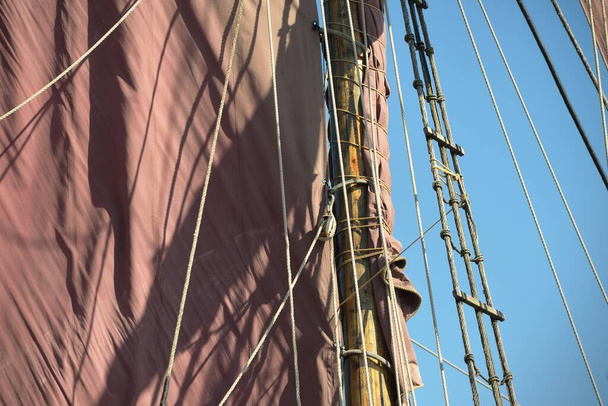 Mast, rode zeilen en tuigage van een oud klassiek zeilschip uit de 18e eeuw, close-up. Heldere blauwe lucht - Foto, afbeelding