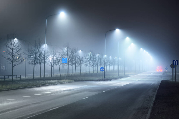 Podświetlana, pusta autostrada we mgle w nocy. Światła uliczne i znaki drogowe z bliska. Ciemna scena miejska, pejzaż miasta. Ryga, Łotwa. Niebezpieczna jazda, prędkość, wolność, obraz koncepcyjny - Zdjęcie, obraz