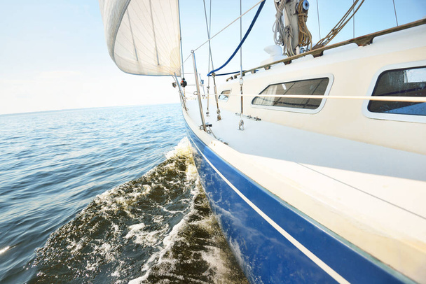 Weiße Jacht segelt an einem sonnigen Sommertag. Nahsicht vom Deck auf Bug und Segel. Wellen und Wasser plätschern. Strahlend blauer Himmel. Ostsee, Schweden - Foto, Bild