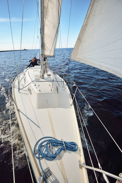A couple of people on the white yacht sailing on a clear day. Top down view from the bow to the deck, mast and sails. Recreation and summer sport theme. Ruhnu island, Estonia - Photo, Image
