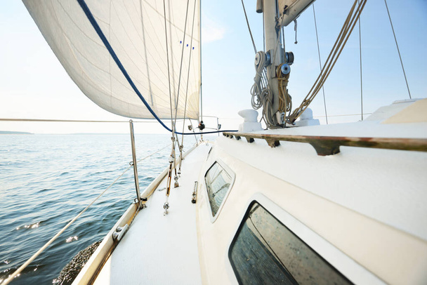 Fehér jacht vitorlázás egy napos nyári napon. Közelkép a fedélzetről az orrra és a vitorlákra. Hullámok és vízcsobbanások. Tiszta kék ég. Balti-tenger, Svédország - Fotó, kép