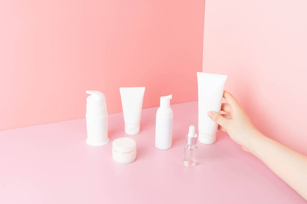 Skincare routine- Women hand choosing skin care products for healthy skin on pink background. Packaging of facial foam, cleansing, essence, serum, cream or lotion. Beauty and cosmetic concept. - Photo, Image
