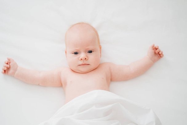 cute red-haired baby lies on a white bed. concept of baby care - Foto, immagini
