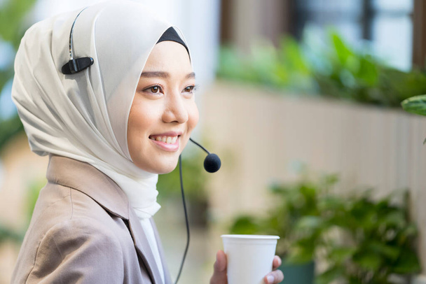 Call center drinking warm water and rest. Muslim call center staff. Young female customer support executive working in office. - Φωτογραφία, εικόνα