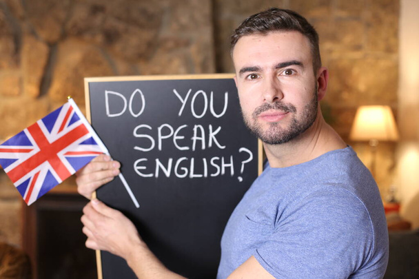портрет красивого молодого человека с флагом Великобритании и доской. Вы говорите по-английски дома? - Фото, изображение