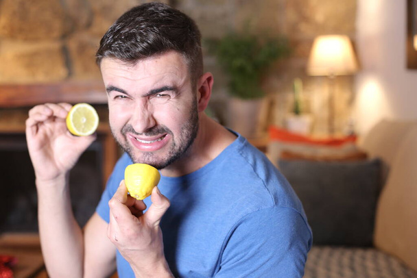portrait of handsome young man licking sour lemon fruit at home - 写真・画像