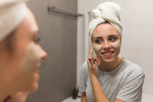 woman applying clay face mask in bathroom at her home - Foto, Imagem