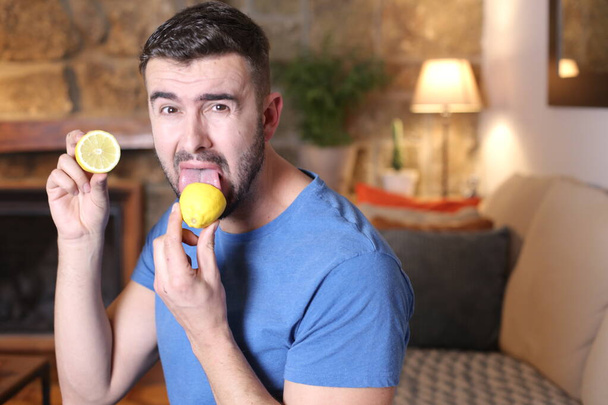 portrait of handsome young man licking sour lemon fruit at home - Foto, Imagen